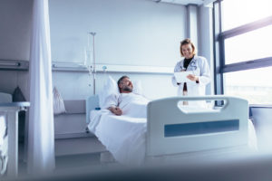 picture of a hospital patient in bed with a dr or nurse standing beside the bed
