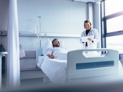 picture of a hospital patient in bed with a dr or nurse standing beside the bed